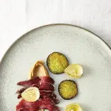 Gebeiztes Rinderfilet mit cremiger Beilage, karamellisierten Zwiebeln und grünen, knusprigen Scheiben auf einem Teller.