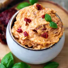 Cremige Tomatenbutter selbst machen: Ein Schälchen mit köstlicher Tomatenbutter, garniert mit Basilikum und getrockneten Tomatenstücken.