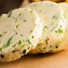 Drei Scheiben Kapuzinerkressebutter liegen auf einem braunen Untergrund. Die Butter ist mit grünen Kräutern durchsetzt.