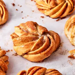 Goldbraune Kardamomschnecken, bestreut mit Zucker und Zimt, liegen auf Backpapier.