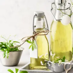 Zwei Flaschen mit omas waldmeistersirup, verziert mit frischen Waldmeisterzweigen und kleinen weißen Blüten.