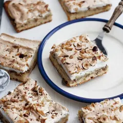 Saftiger Apfelkuchen mit Boskop-Äpfeln und Baiserhaube, bestreut mit gehackten Nüssen. Ein Stück auf einem Teller, bereit zum Genuss.