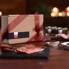 Geschenkbox mit Wurstwaren und Pastete, dazu ein Glas mit Gewürzen und ein Gericht mit Fleisch. Perfekt zu einem Glas **amber ale**.