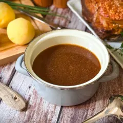 Ein Topf mit köstlichem Bratenfond, bereit, um das Gericht zu verfeinern. Daneben liegen gekochte Kartoffeln und ein Stück Braten.