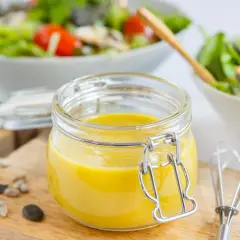 Frische, selbstgemachte Salatsauce im Glas, bereit für den Salat. Mit Kernen und einem kleinen Schneebesen daneben.