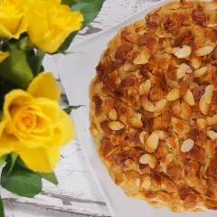 Ein köstlicher bienenstich ohne sahne, bedeckt mit gerösteten Mandelblättchen, neben einem Strauß gelber Rosen.