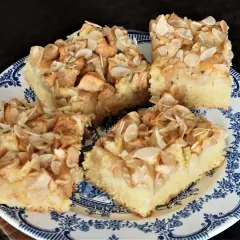 Vier Stücke saftiger Apfelkuchen vom Blech mit Mandeln, auf einem blauen Teller angerichtet.