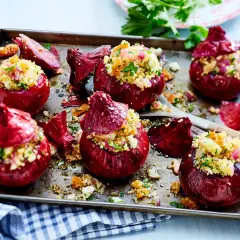 Gebackene Zwiebeln, gefüllt mit Couscous und Kräutern, auf einem Backblech.