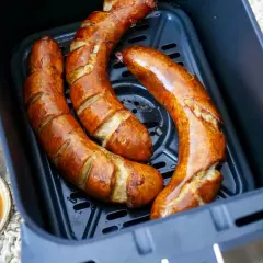 Drei goldbraune Bratwürste in der Friteuse, bereit zum Genießen. Daneben eine Schale mit Dip und frische Petersilie.
