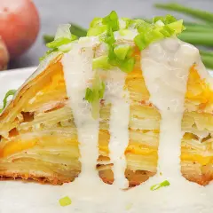 Ein Stück Kartoffelkuchen nach altem Rezept, geschichtet mit Käse und überzogen mit cremiger Sauce und Frühlingszwiebeln.