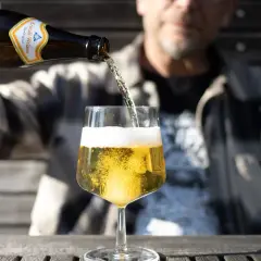 Mann schenkt helles Bier ein. Die Schaumkrone ist üppig. Wer auf Bier Kalorien achtet, wählt oft ein helles Weizen.