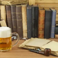 Ein Glas **Saison Bier** steht neben alten Büchern und einer Pfeife.