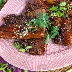 Glasierter schweinebauch asiatisch, garniert mit Frühlingszwiebeln und Sesam. Rote Chilischoten und Koriander runden das Gericht ab.