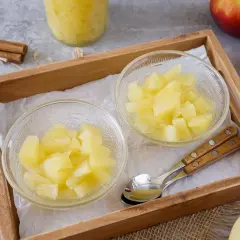 Zwei Schalen mit selbstgemachtem Apfelkompott, daneben Äpfel und Zimtstangen. Ein Löffel liegt bereit.