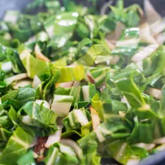Bunter Mangold braten in der Pfanne. Grüne Blätter und weiße Stiele werden gedünstet, Dampf steigt auf.