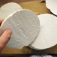 Ein Mensch hält eine dicke Scheibe eines riesigen Bovists, bereit für ein leckeres riesenbovist rezept. Mehrere weitere Scheiben liegen auf einem Holzbrett.