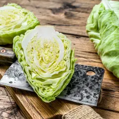 Frischer spitzkohl roh, halbiert und auf einem Holzbrett mit einem Hackmesser. Bereit für die Zubereitung eines knackigen Salats.