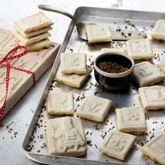 Holzmodel für Springerle backen, daneben frisch gebackene Kekse mit verschiedenen Motiven auf einem Blech.