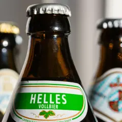 Drei Bierflaschen, eine mit "Helles Vollbier" beschriftet. Der Unterschied zwischen Vollbier und hellem Bier wird hier visuell angedeutet.