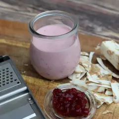 Meerrettichschmand in einem Glas, daneben frisch geriebener Meerrettich, eine Reibe und Preiselbeeren.