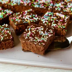 Saftiger schokokuchen blech mit bunten Streuseln, bereit zum Servieren. Ein Stück wird gerade mit einem Tortenheber herausgenommen.