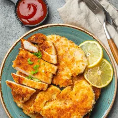 Knusprige Schnitzel mit Treber Panade, garniert mit Zitrone und Schnittlauch, daneben eine Schale Ketchup.