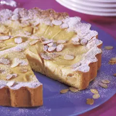 Ein köstlicher Apfelkuchen mit Guss, bestreut mit Puderzucker und Mandelblättchen, auf einem blauen Teller.