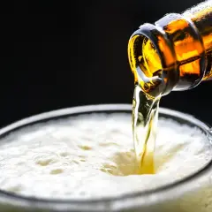 Ein bernsteinfarbenes alkoholfreies Bier fließt aus einer Flasche in ein Glas mit viel Schaum. Perfekt für alle, die alkoholfreies Bier selber brauen möchten.