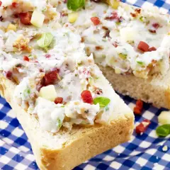 Schmalz-Brotaufstriche mit Speck und Kräutern auf rustikalem Brot, serviert auf blau-weiß karierter Platte.