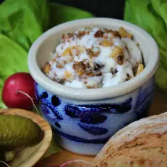 Griebenschmalz, ein traditionelles Gericht, in einem blauen Steingut-Napf, serviert mit Brot, Radieschen und Gewürzgurken.
