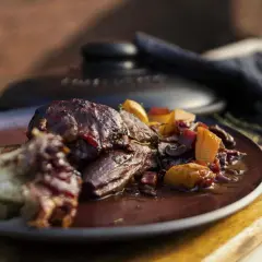 Ein saftiges Lammhaxe Rezept, serviert mit Wurzelgemüse in einer dunklen Sauce auf einem Teller.