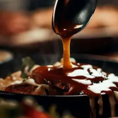 Ein Löffel übergießt ein Gericht mit einer glänzenden, dunklen Sauce. Ein köstliches dunkle sauce rezept zum Nachmachen.