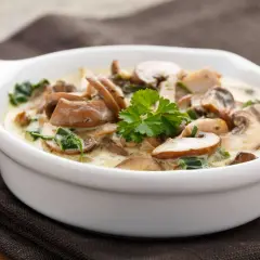 Cremige Pilzpfanne mit Speck und frischer Petersilie in einer weißen Schüssel.