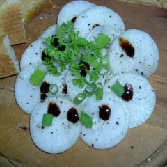 Frisch geschnittener Radi mit Kräutern und dunklem Balsamico auf Holzbrett, dazu Baguette.