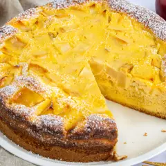 Ein schneller, saftiger Apfelkuchen mit Quark, bestäubt mit Puderzucker. Daneben liegen Äpfel und goldene Gabeln.
