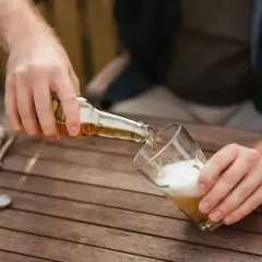 Mann schenkt Bier ein. Vielleicht für ein 20-Liter-Bier-Rezept? Ein Kronkorken und ein Flaschenöffner liegen bereit.