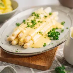 Spargel mit cremiger Sauce Hollandaise, ein Klassiker, der mit diesem Rezept gelingt. Beilagen wie Kartoffeln sind im Hintergrund zu sehen.