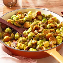 Gebratener Rosenkohl in einer Pfanne, mit Kräutern bestreut und einer Holzschaufel zum Servieren.