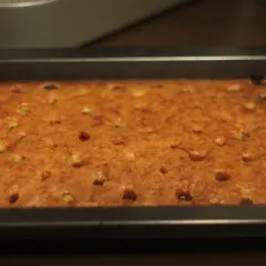 Frisch gebackener, goldbrauner tante mathildas kirschkuchen in einer rechteckigen Backform. Kleine Kirschstücke sind im Teig verteilt.