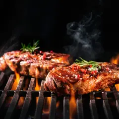 Zwei saftige Steaks brutzeln auf dem Grill, verfeinert mit einer Schwarzbier-Marinade, Rosmarin und rosa Pfeffer.