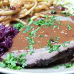 Sauerbraten einlegen rotwein: zarte Scheiben Fleisch in dunkler Soße, dazu Rotkohl und Nudeln.