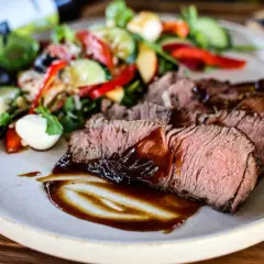 Saftiges Roastbeef als Beilage mit einem frischen Salat aus Tomaten, Gurken, Paprika und Mozzarella-Kugeln, beträufelt mit dunkler Sauce.