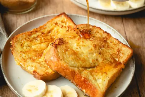 Arme Ritter, goldbraun gebraten, werden mit Sirup übergossen. Dazu Bananenscheiben und brauner Zucker.