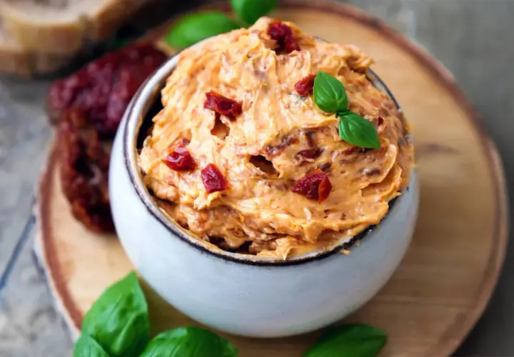 Cremige Tomatenbutter selbst machen: Ein Schälchen mit köstlicher Tomatenbutter, garniert mit Basilikum und getrockneten Tomatenstücken.
