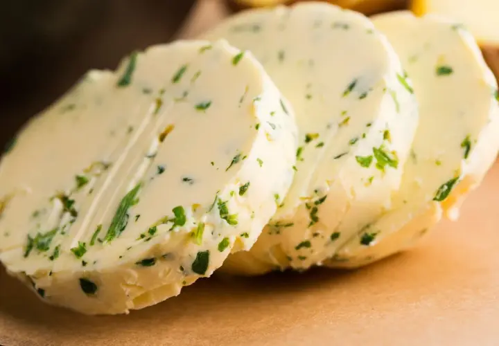 Drei Scheiben Kapuzinerkressebutter liegen auf einem braunen Untergrund. Die Butter ist mit grünen Kräutern durchsetzt.