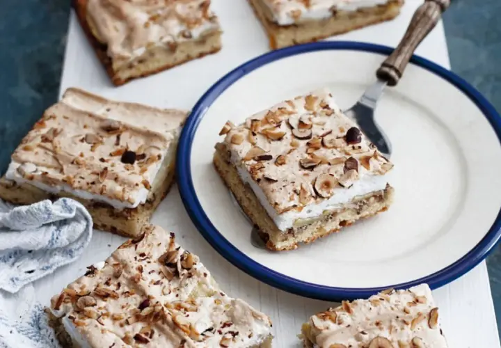 Saftiger Apfelkuchen mit Boskop-Äpfeln und Baiserhaube, bestreut mit gehackten Nüssen. Ein Stück auf einem Teller, bereit zum Genuss.