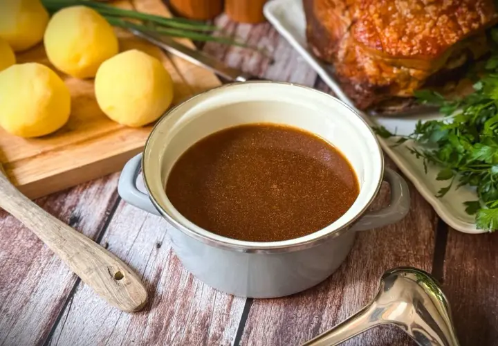 Ein Topf mit köstlichem Bratenfond, bereit, um das Gericht zu verfeinern. Daneben liegen gekochte Kartoffeln und ein Stück Braten.