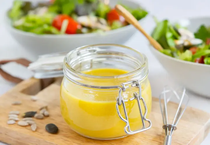 Frische, selbstgemachte Salatsauce im Glas, bereit für den Salat. Mit Kernen und einem kleinen Schneebesen daneben.