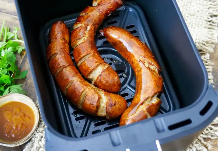 Drei goldbraune Bratwürste in der Friteuse, bereit zum Genießen. Daneben eine Schale mit Dip und frische Petersilie.