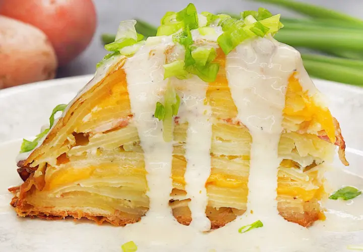 Ein Stück Kartoffelkuchen nach altem Rezept, geschichtet mit Käse und überzogen mit cremiger Sauce und Frühlingszwiebeln.